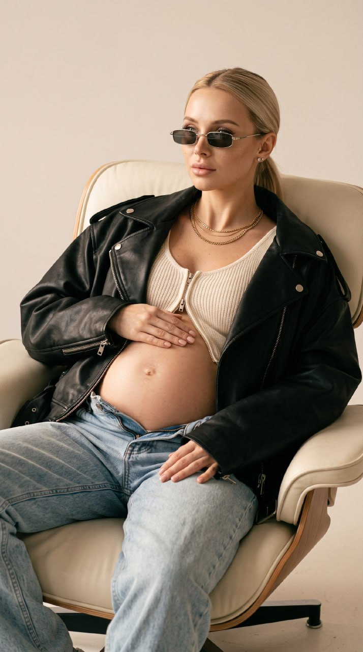 ИИ-фотосессия по фото: беременная девушка в черной кожаной куртке, светлом топе и солнцезащитных очках сидит в кресле.