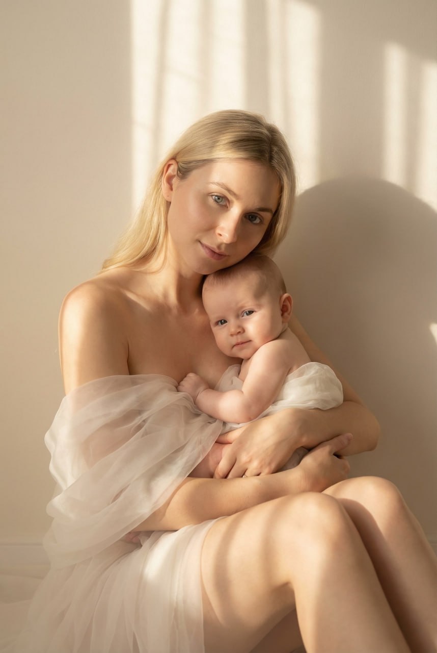 ИИ-фотосессия по фото: нежный портрет матери с младенцем на руках, укутанных в легкую светлую ткань. Мягкие золотистые тени и теплый бежевый фон.