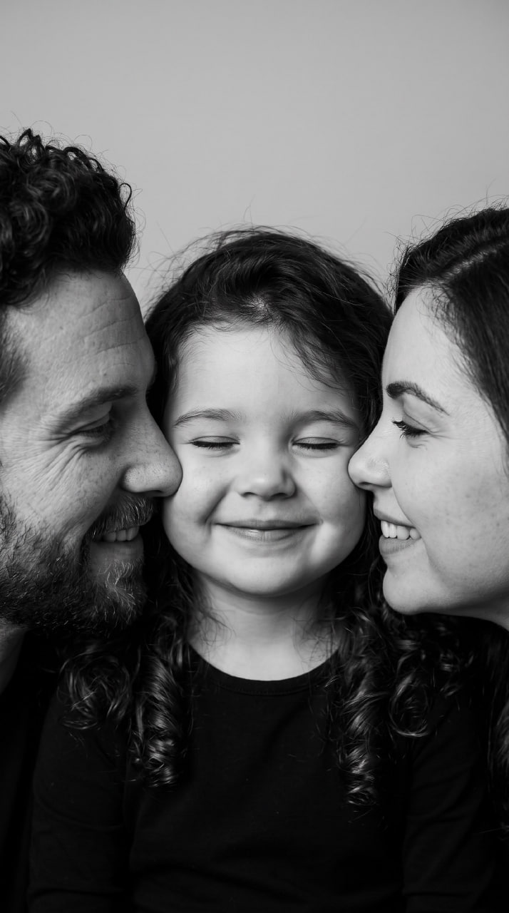 ИИ-фотосессия по фото: черно-белый студийный портрет крупным планом, где родители нежно прижимаются к щекам улыбающейся дочки.