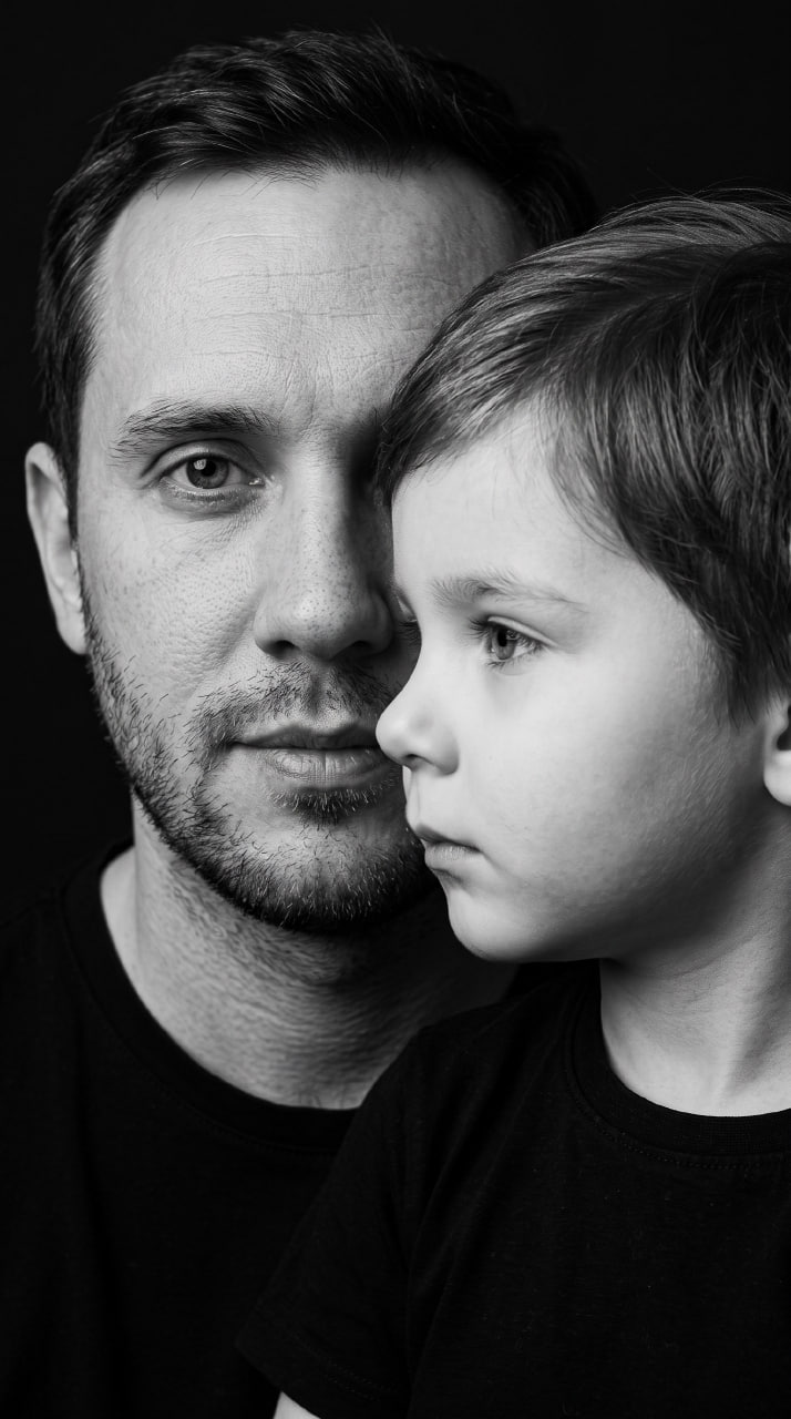 ИИ-фотосессия по фото: черно-белый крупный план мужчины и мальчика в черных футболках на темном студийном фоне.
