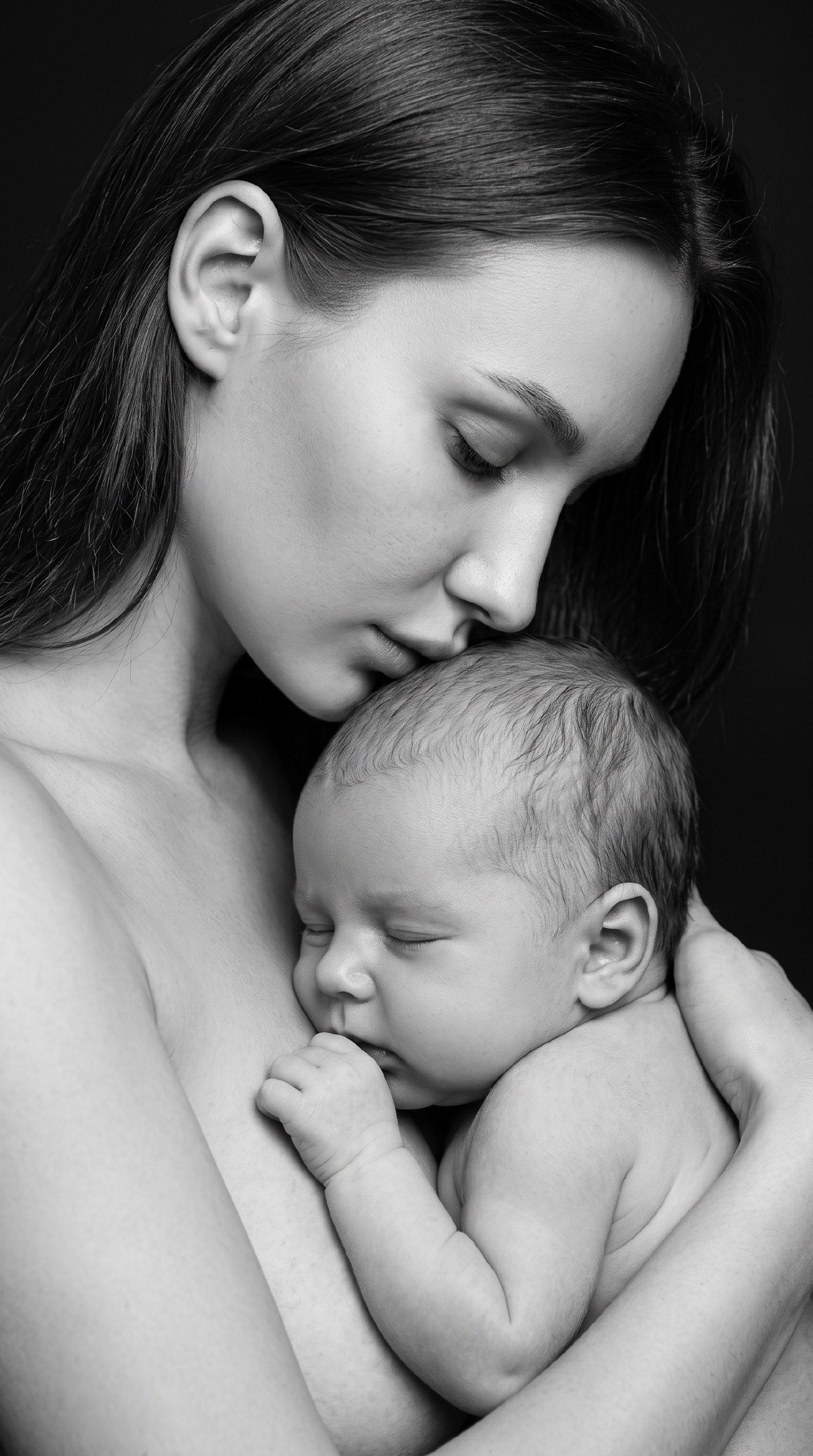 ИИ-фотосессия по фото: крупный черно-белый студийный портрет мамы, нежно целующей спящего младенца на темном фоне.
