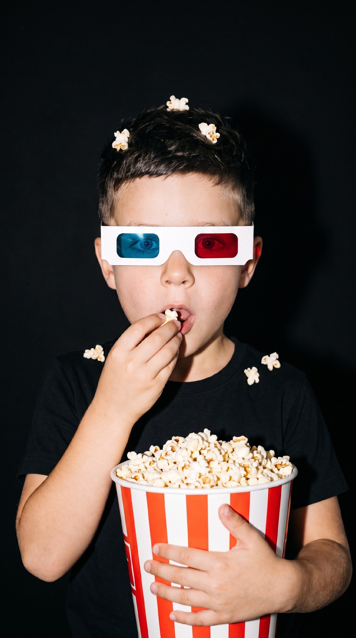 ИИ-фотосессия по фото: ребенок в картонных 3D-очках и черной футболке держит полосатое ведерко с попкорном на черном фоне со вспышкой.